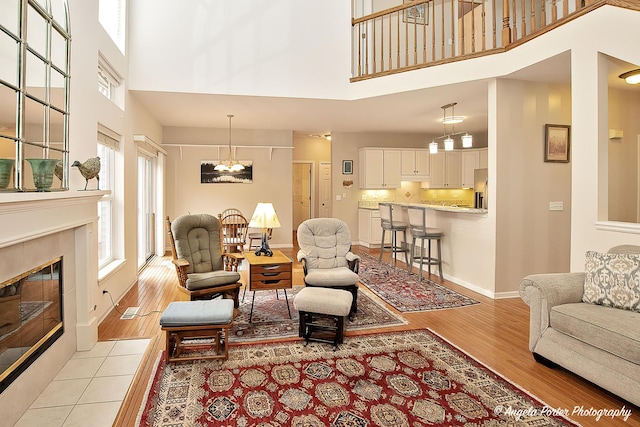 living room featuring a high ceiling, a tiled fireplace, a chandelier, light wood-type flooring, and baseboards