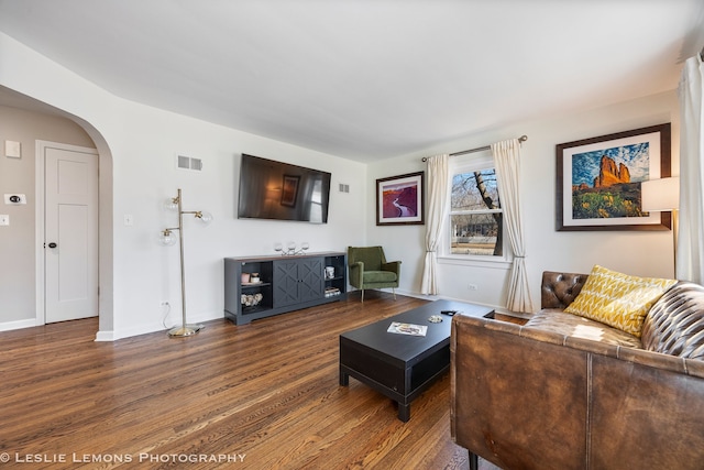 living room featuring visible vents, arched walkways, dark wood finished floors, and baseboards