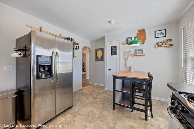 kitchen featuring range with gas cooktop, arched walkways, baseboards, and stainless steel fridge with ice dispenser