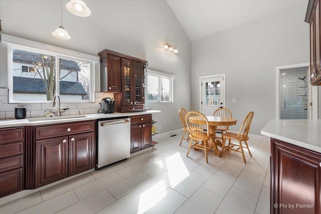 kitchen with a sink, stainless steel dishwasher, light countertops, glass insert cabinets, and baseboards