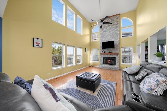 living room with a stone fireplace, baseboards, light wood-style floors, and a ceiling fan