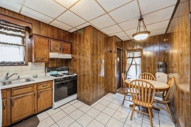 kitchen featuring under cabinet range hood, a sink, a wealth of natural light, brown cabinets, and gas range