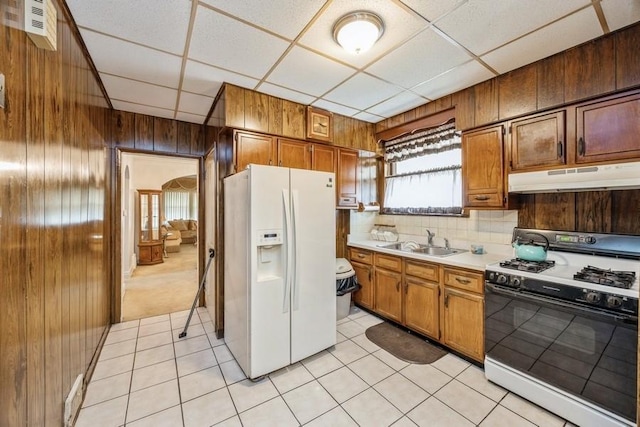 kitchen with light countertops, under cabinet range hood, white fridge with ice dispenser, a sink, and gas stove