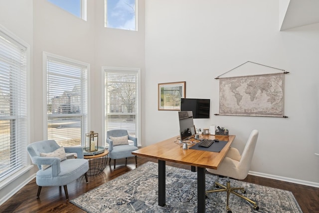 office space with a towering ceiling, baseboards, visible vents, and wood finished floors