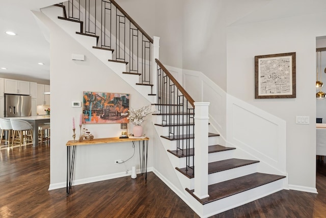 stairway featuring baseboards, a decorative wall, wood finished floors, and recessed lighting