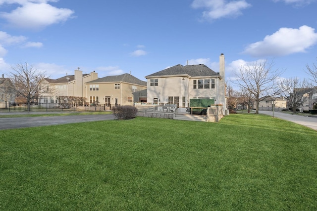 rear view of house with a yard, a chimney, fence, and a residential view