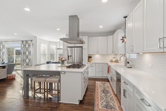 kitchen with island exhaust hood, a kitchen island, white cabinets, appliances with stainless steel finishes, and a kitchen bar