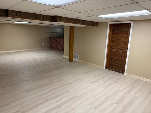 finished below grade area featuring baseboards, a drop ceiling, visible vents, and light wood-style floors