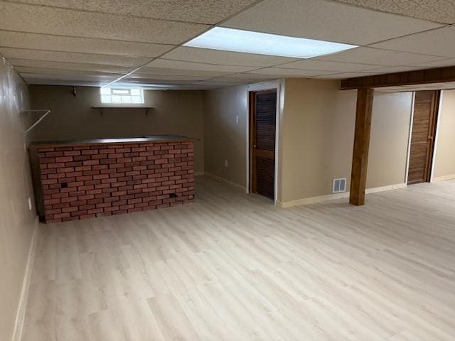 basement with a drop ceiling, wood finished floors, visible vents, and baseboards