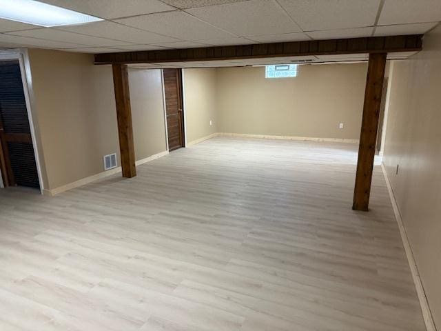 basement with light wood-type flooring, visible vents, a drop ceiling, and baseboards