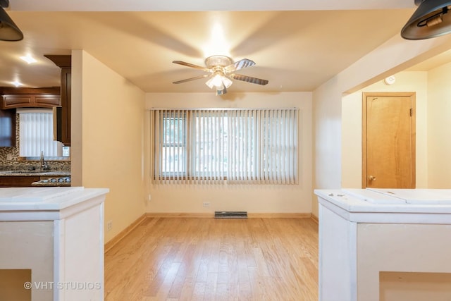 interior space featuring a ceiling fan, a sink, light wood-style flooring, and baseboards