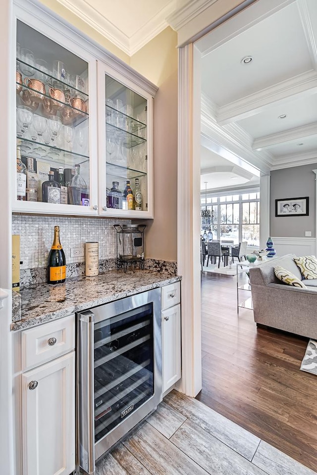 bar featuring backsplash, wine cooler, a dry bar, ornamental molding, and light wood-style flooring