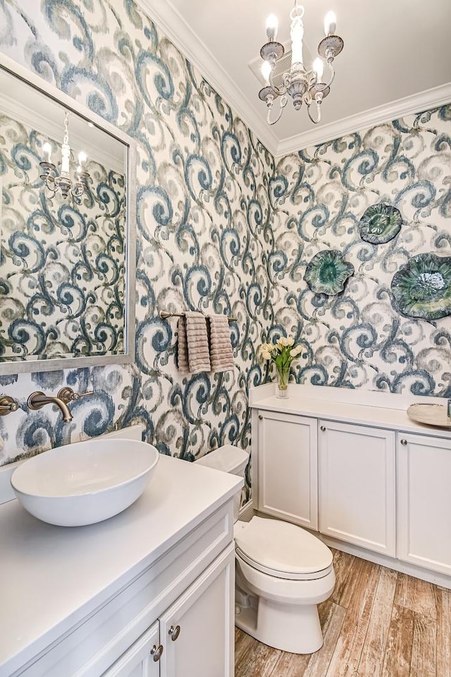 bathroom with wallpapered walls, crown molding, toilet, a notable chandelier, and vanity