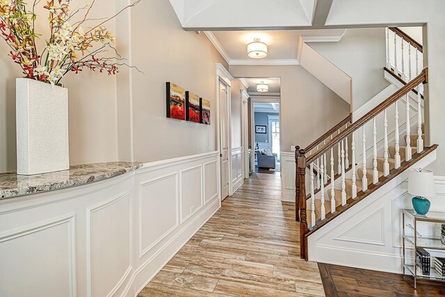 entrance foyer featuring stairs, ornamental molding, wainscoting, light wood-style flooring, and a decorative wall