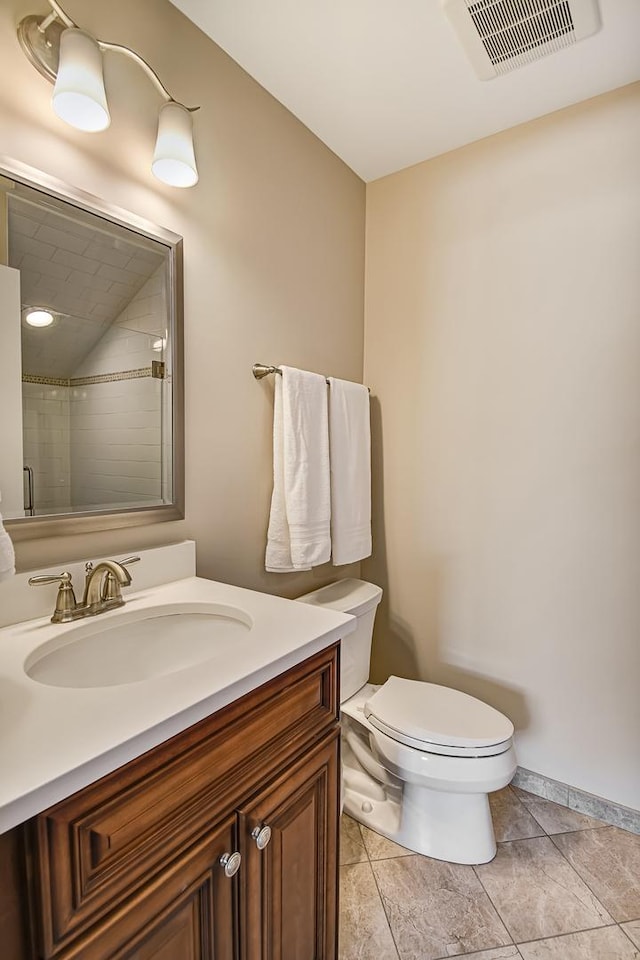 bathroom with visible vents, toilet, baseboards, tiled shower, and vanity