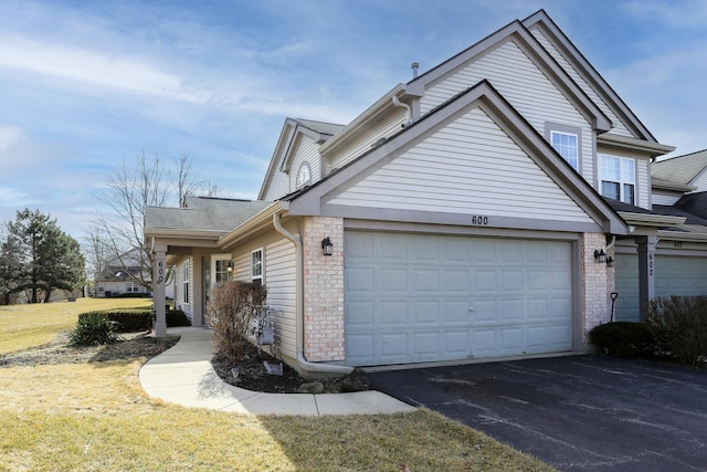 view of side of property featuring an attached garage, aphalt driveway, a lawn, and brick siding