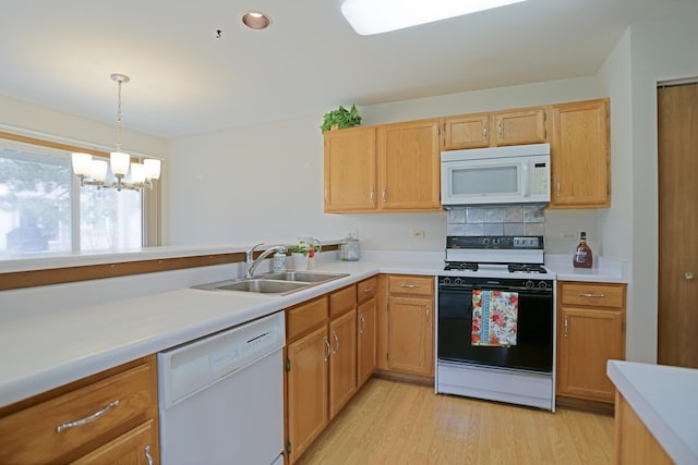 kitchen featuring light wood finished floors, light countertops, decorative backsplash, a sink, and white appliances