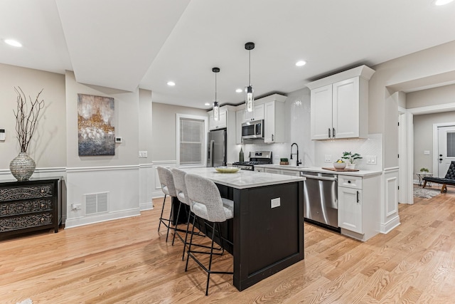 kitchen featuring visible vents, a kitchen breakfast bar, a center island, stainless steel appliances, and white cabinetry