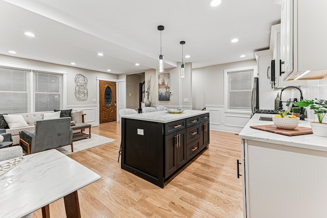 kitchen featuring light wood finished floors, open floor plan, white cabinets, a sink, and dark cabinets