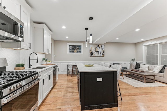 kitchen featuring stainless steel appliances, a sink, white cabinets, wainscoting, and a center island