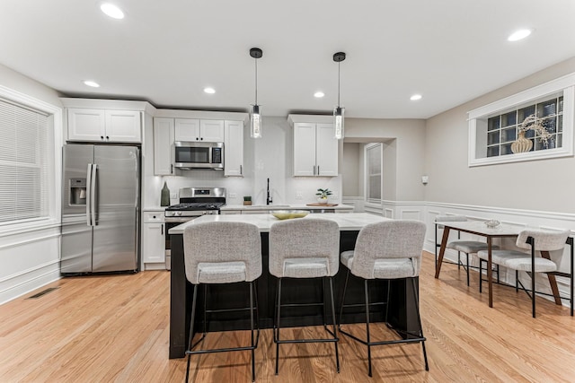 kitchen featuring stainless steel appliances, a kitchen island, light wood-style flooring, and a breakfast bar area