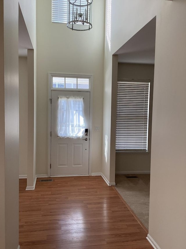 entryway featuring an inviting chandelier, wood finished floors, a towering ceiling, and baseboards