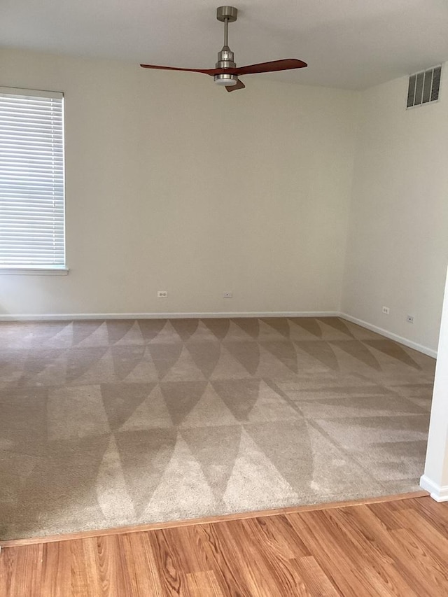 carpeted empty room featuring visible vents, ceiling fan, baseboards, and wood finished floors