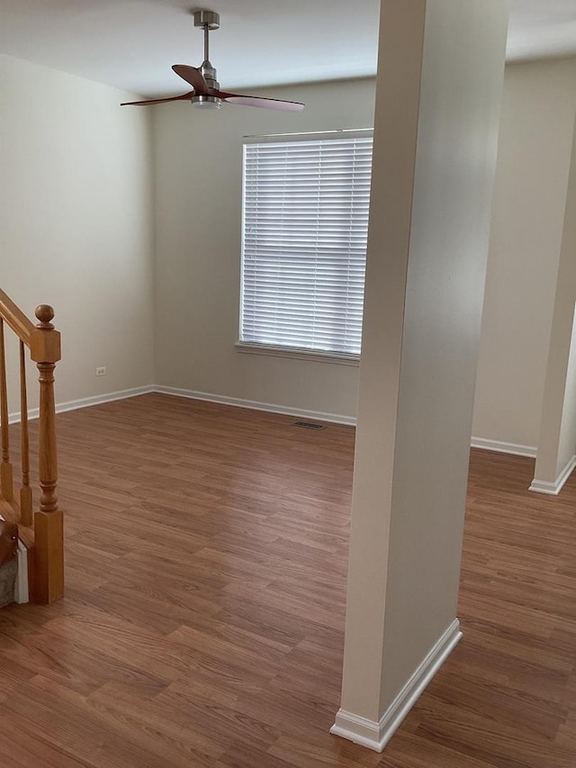 empty room with a ceiling fan, wood finished floors, baseboards, and stairs