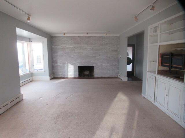 unfurnished living room featuring built in shelves, a large fireplace, a baseboard heating unit, carpet, and track lighting