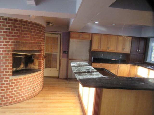 kitchen with dark countertops, light wood finished floors, and a brick fireplace