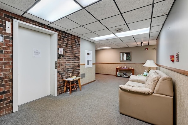 carpeted living area featuring a wainscoted wall and a drop ceiling