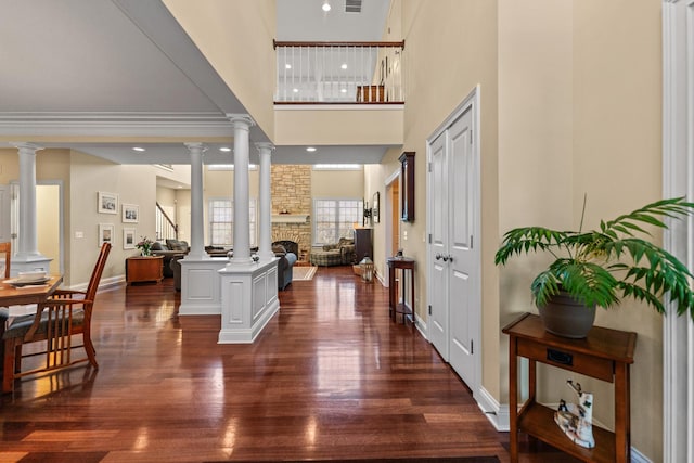 foyer with a stone fireplace, dark wood-style floors, and ornate columns