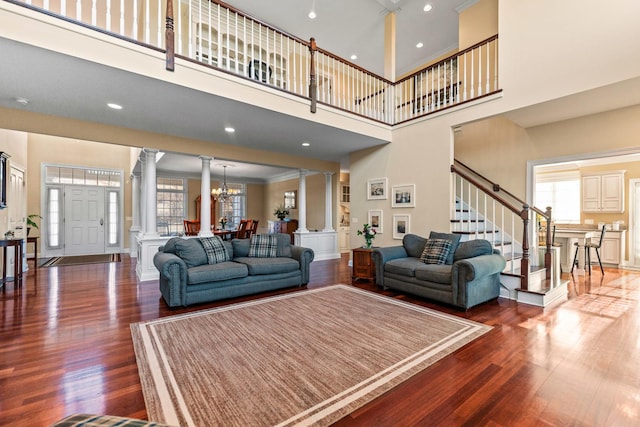 living area featuring stairs, an inviting chandelier, wood finished floors, and ornate columns