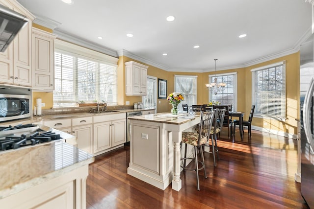 kitchen with a kitchen island, ornamental molding, stainless steel appliances, and a sink