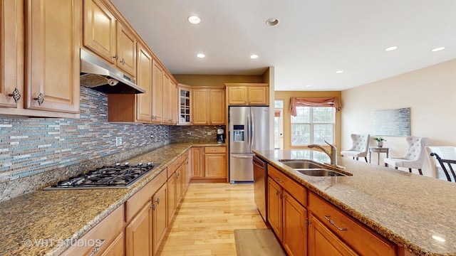 kitchen with stainless steel appliances, stone countertops, light wood-style floors, a sink, and under cabinet range hood