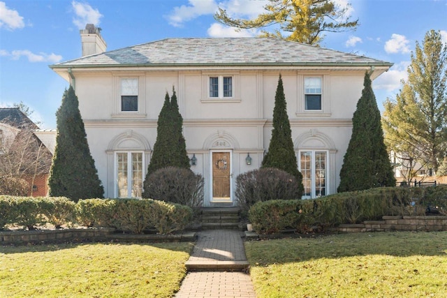 view of front of property with stucco siding, a chimney, and a front yard