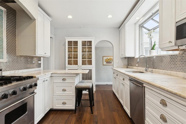 kitchen featuring dark wood-style flooring, appliances with stainless steel finishes, white cabinetry, a sink, and light stone countertops