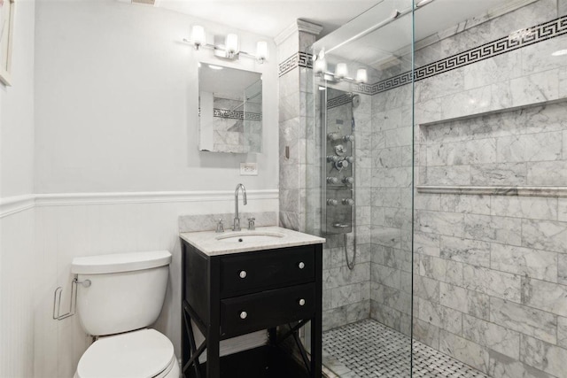 bathroom featuring toilet, a wainscoted wall, a tile shower, and vanity