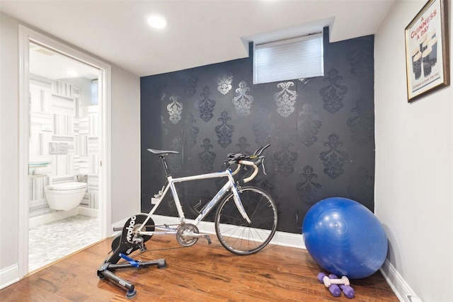 exercise room featuring an accent wall, wood finished floors, baseboards, and wallpapered walls