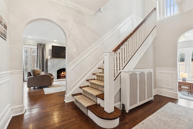 stairway with arched walkways, a fireplace, a decorative wall, and wood finished floors