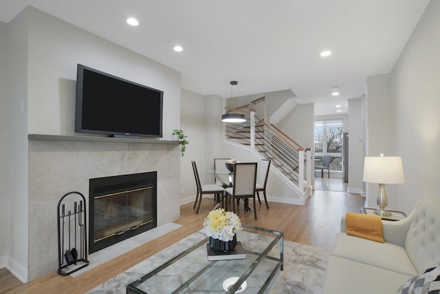 living room featuring baseboards, stairway, light wood-type flooring, a fireplace, and recessed lighting