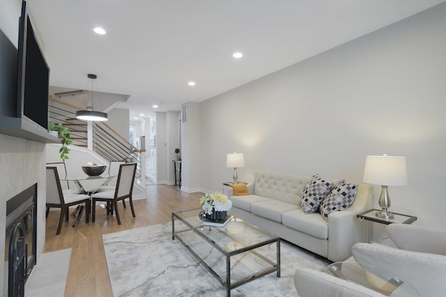 living room featuring recessed lighting, light wood-style flooring, a fireplace with flush hearth, baseboards, and stairs