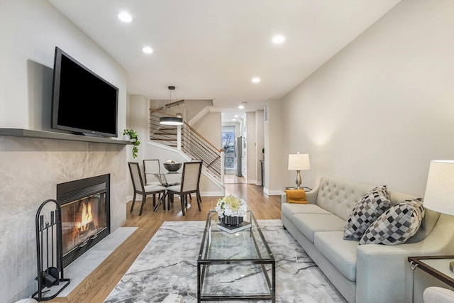 living room with light wood finished floors, baseboards, a high end fireplace, stairway, and recessed lighting