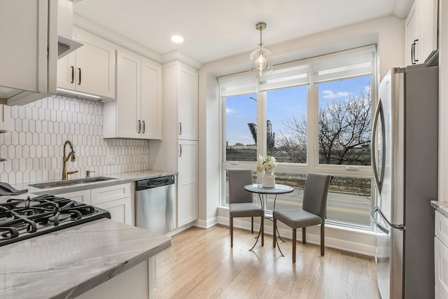 kitchen featuring light stone counters, stainless steel appliances, light wood-style flooring, decorative backsplash, and white cabinets