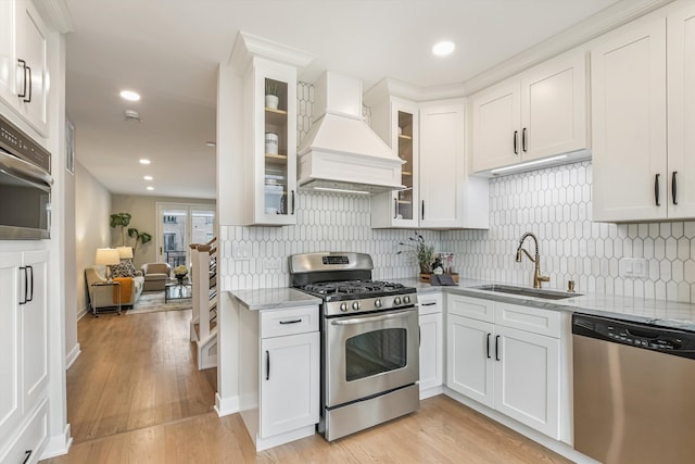 kitchen with light wood-style flooring, appliances with stainless steel finishes, a sink, light stone countertops, and premium range hood