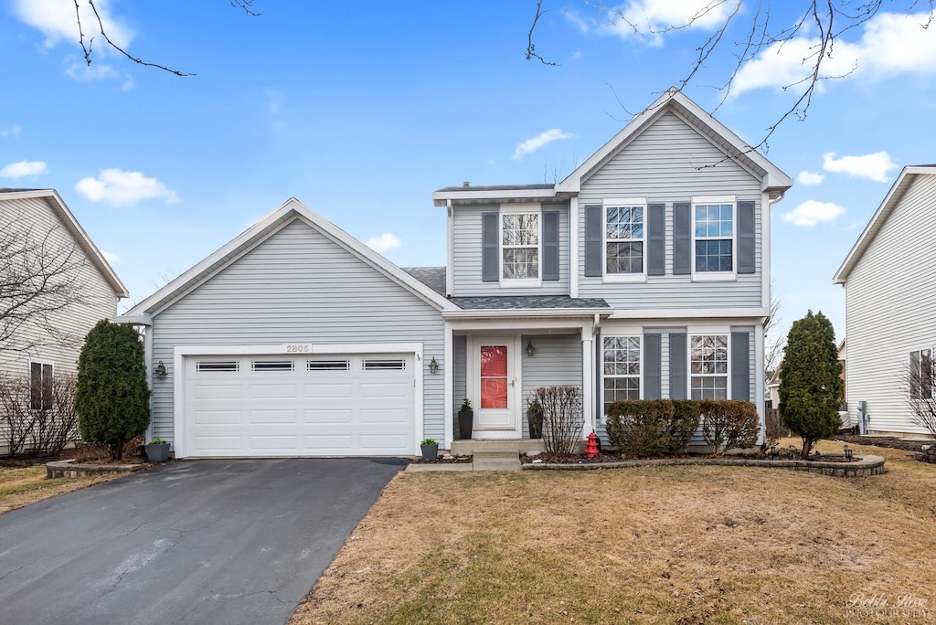 traditional home featuring aphalt driveway, an attached garage, and a front yard