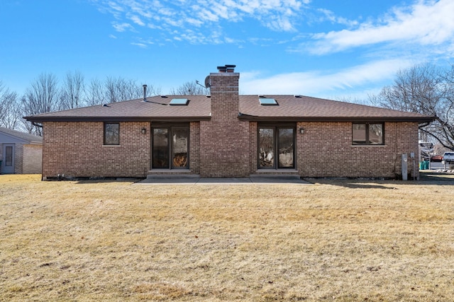 rear view of house featuring a shingled roof, a lawn, a chimney, a patio area, and brick siding