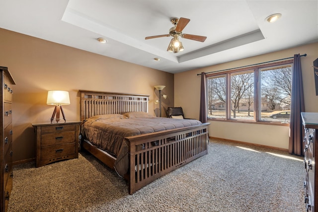 bedroom featuring ceiling fan, carpet floors, a tray ceiling, and baseboards