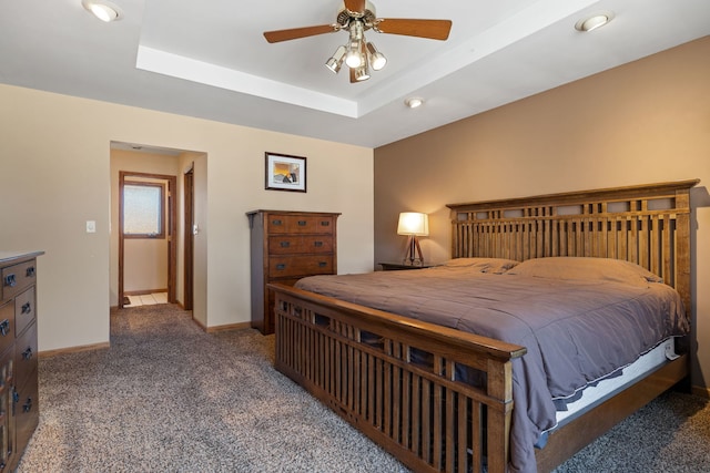 carpeted bedroom with ceiling fan, a tray ceiling, and baseboards