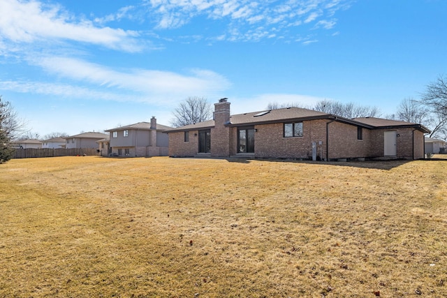 rear view of house featuring a yard, a chimney, and brick siding